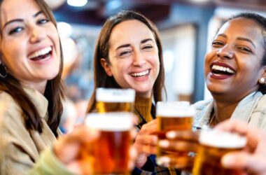 A group of 3 girl smiling and holding glasses of beer